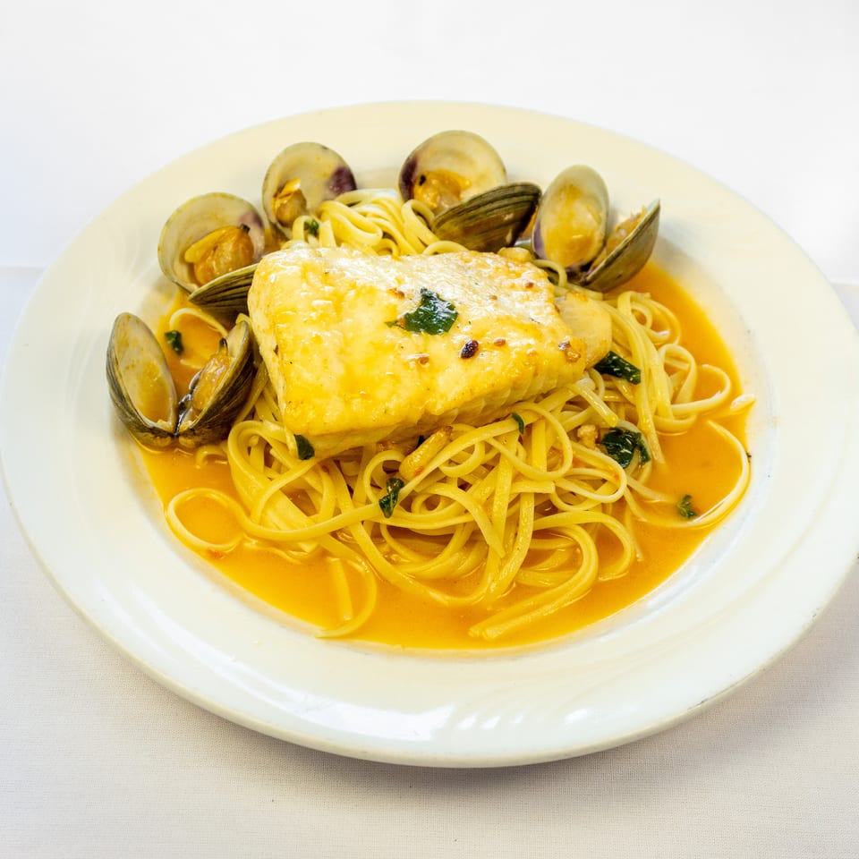 Grilled fish fillet and clams served over linguine in a vibrant orange seafood sauce.