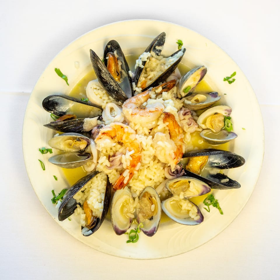 Plate of seafood rice topped with shrimp, mussels, clams, squid, and parsley in a light broth.