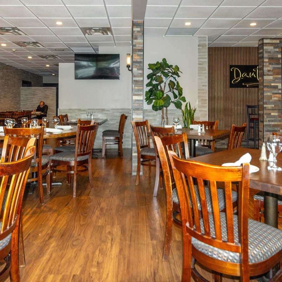 Spacious restaurant dining room with wood tables, upholstered chairs, place settings, plants, stone accents, and two diners.