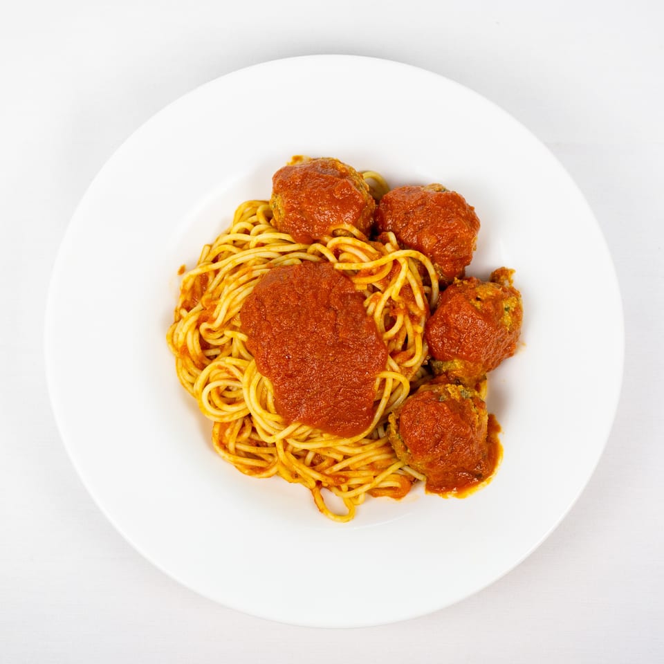 Plate of spaghetti topped with tomato sauce and several meatballs on a white tablecloth.