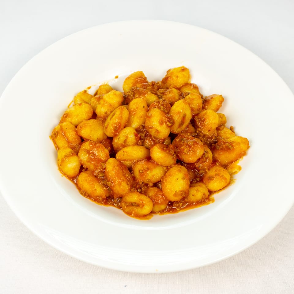 Plate of golden gnocchi tossed in a rich tomato and meat sauce.