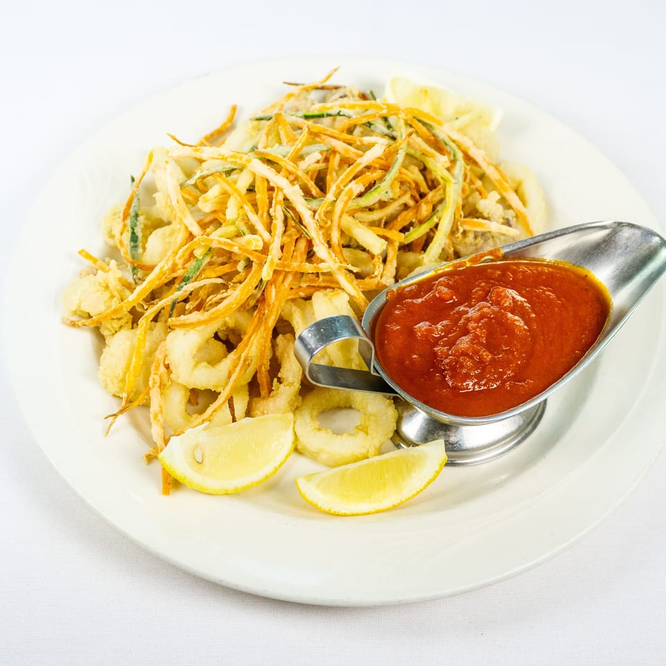 Crispy fried calamari topped with julienned vegetables, served with lemon wedges and marinara sauce on a white plate.