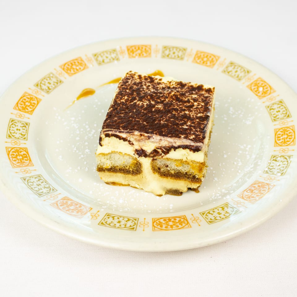 Square slice of tiramisu dusted with powdered sugar on a decorative plate.