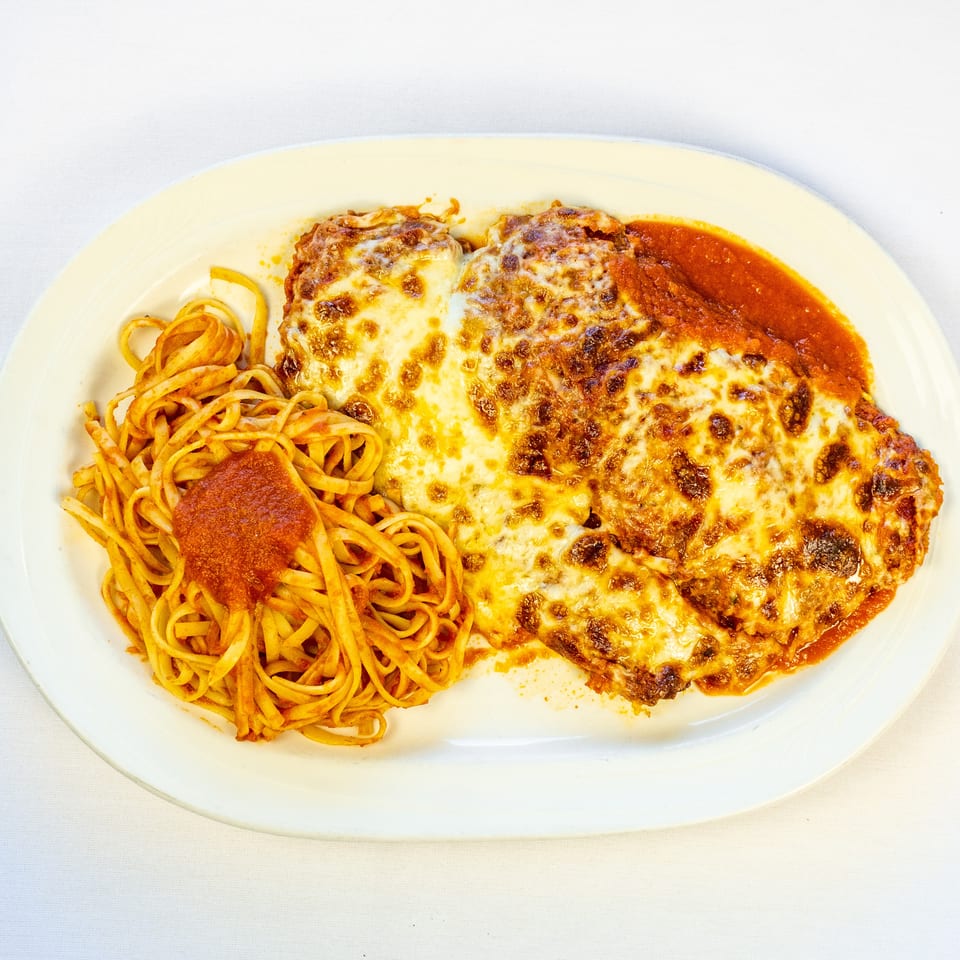Cheesy baked chicken parmesan served with spaghetti and tomato sauce on a white oval plate.