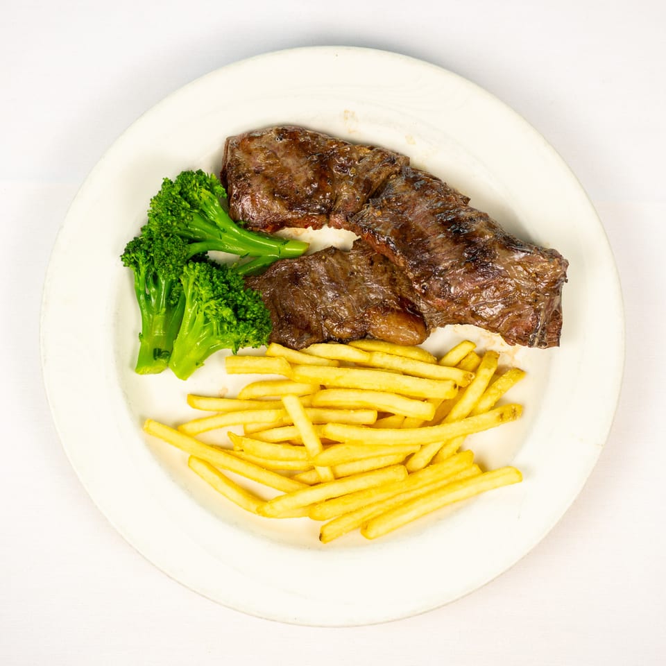 Grilled steak served with French fries and steamed broccoli on a white plate.