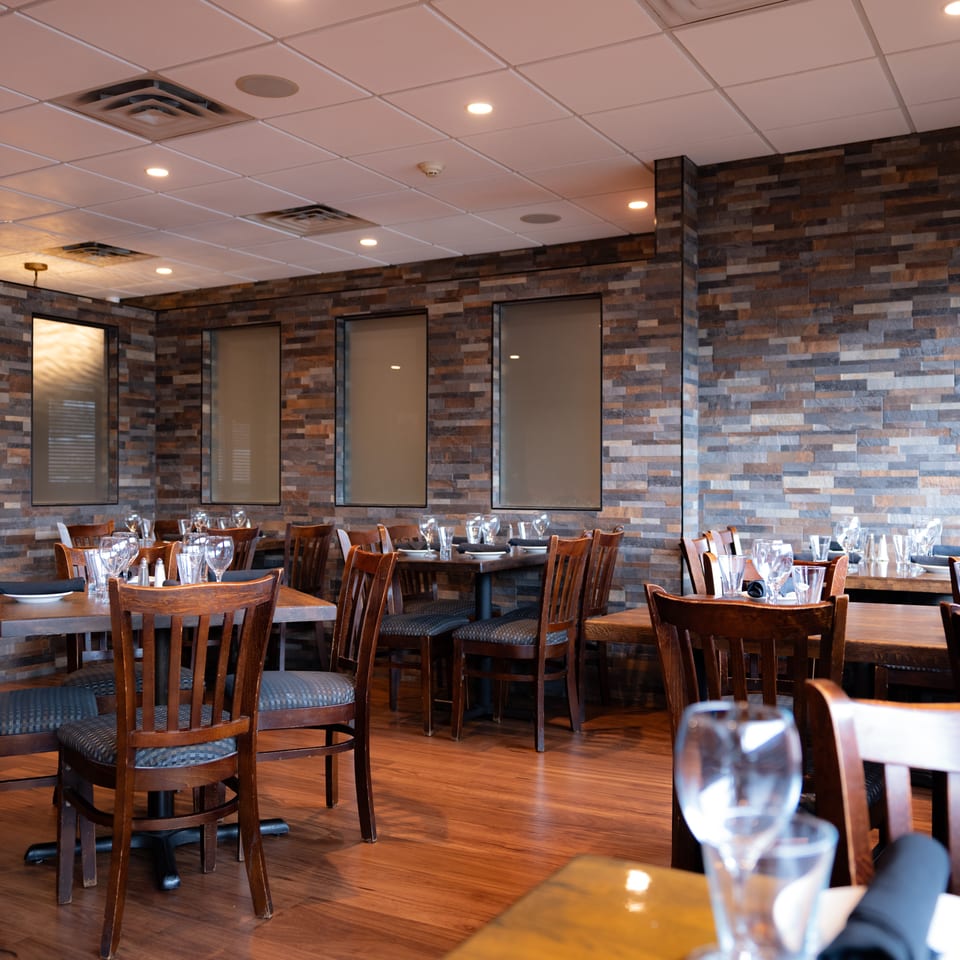 Warm, modern restaurant dining room with wood tables, set wine glasses, dark chairs, stone accent walls, and illuminated Darték sign.
