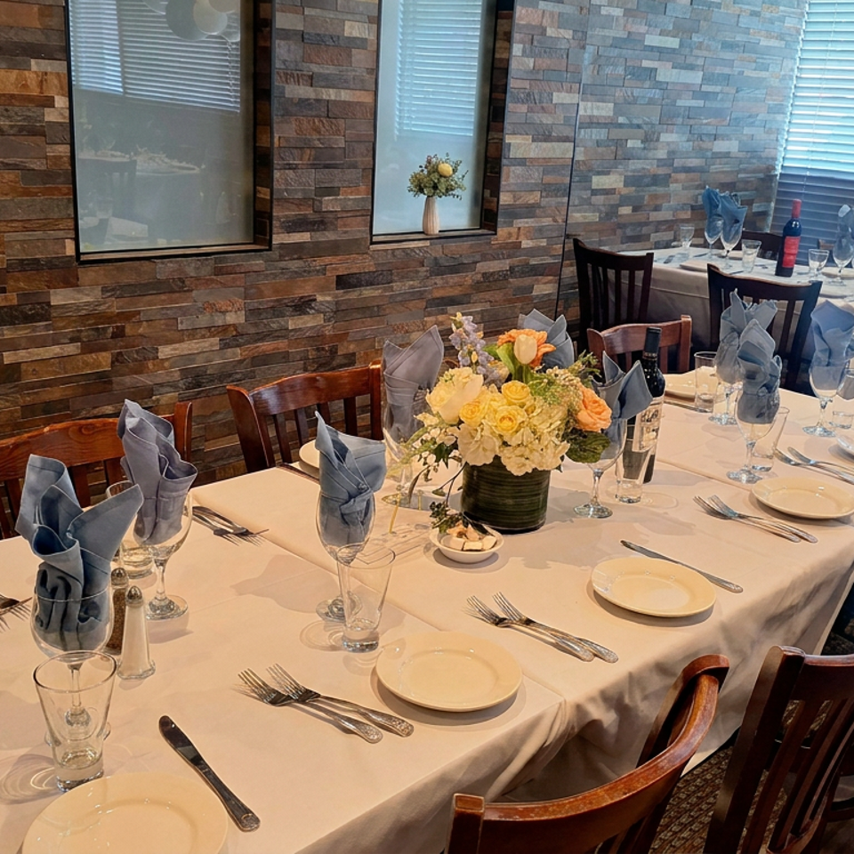 Elegant restaurant dining room with white tablecloths, blue napkins, floral centerpieces, place settings, and warm stone walls.